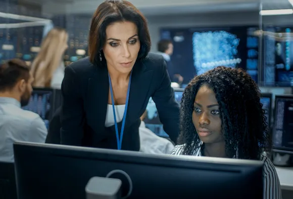 A supervisor looking over the screen of a team member, offering guidance or feedback